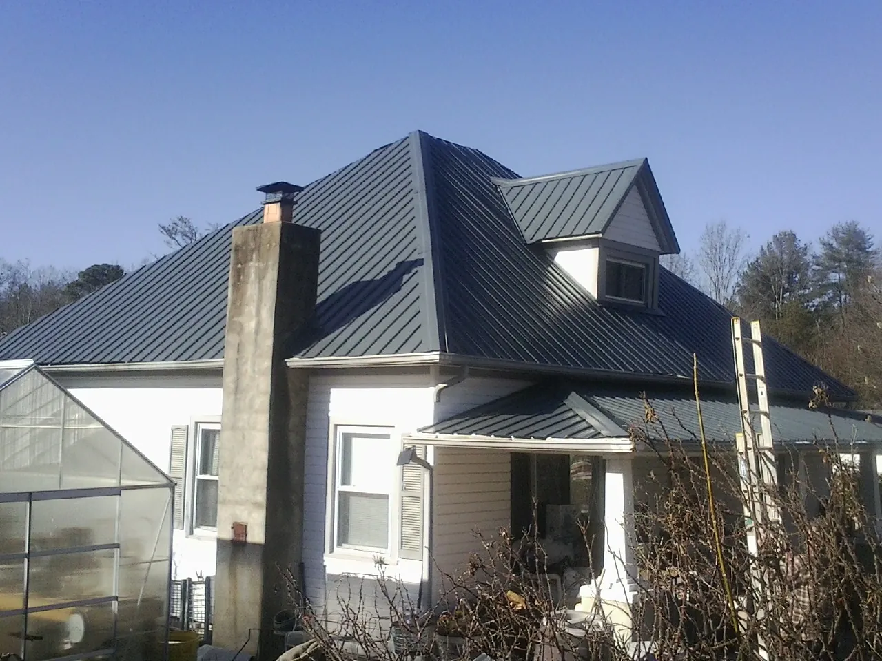 Dark blue standing seam metal roof on a white farmhouse with dormer — Slate & Tile Roof Repair by Roofing Brothers in Westwood