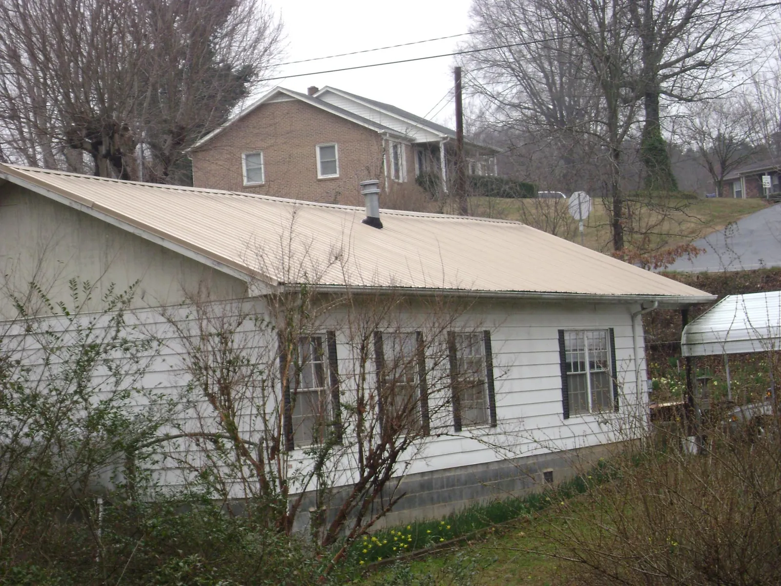 Tan metal roof on a white sided house set into a hillside — Commercial Roofing by Roofing Brothers in Westwood