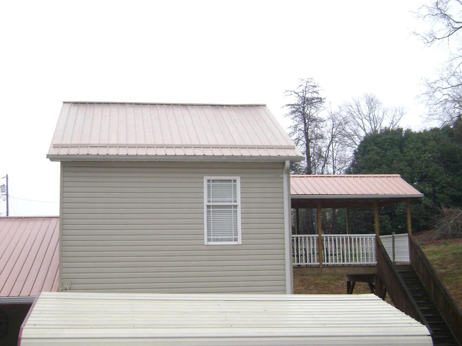 Tan metal roofs on a two story addition and attached porch, from a Roof Replacement job in Westwood